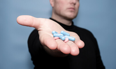 The concept of treatment with antibiotic pills. Medical capsules in a man's hand on a blue background. Medical preparation in tablets. drugs