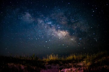 Fototapeta premium Beautiful night sky illuminated with stars and Milky Way galaxy, over a sandy beach dune