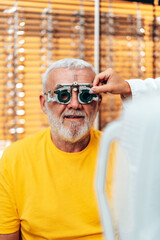 Positive senior male patient checking vision at modern ophthalmology clinic with optical trial frames.