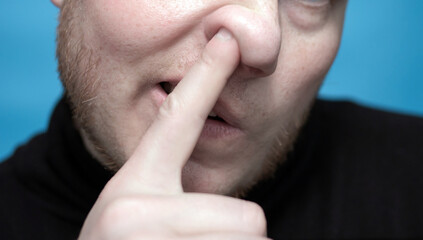 The man picks his nose. Close-up of a man with a finger in his nose.