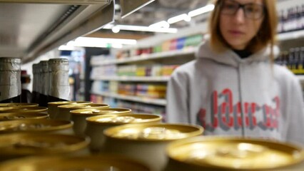 Close-up of many golden beer cans in a supermarket and a young woman takes two