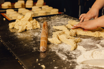 Baker shapes dough on professional metal table in bakery kitchen