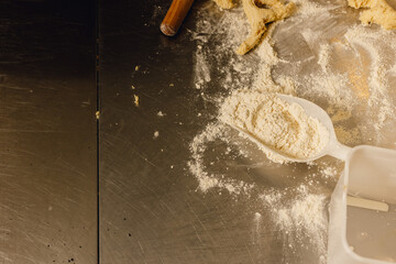 Flour scoop sits on floury bakery table with dough scraps and rolling pin in professional kitchen