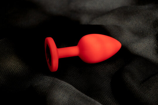 Red silicone anal plug, sex toy, on a black background in the shade. Contrast photo of anal toys, erotic toys