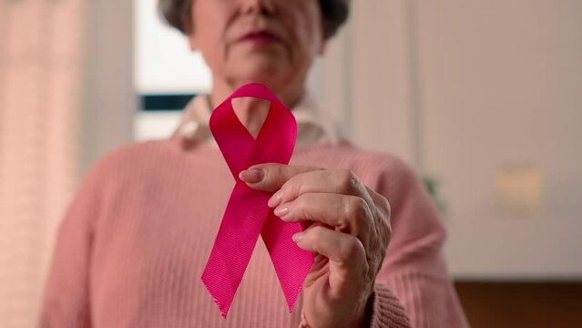 Old senior ill sick woman retired pensioner mature female lady hold red ribbon HIV AIDS awareness disease prevention sign volunteering charity symbol world breast cancer day volunteer oncology support
