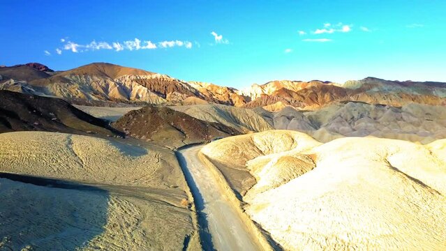Aerial Upward Shot Of Road Amidst Rock Formations At Desert Against Sky, Drone Flying Backward Over Landscape On Sunny Day - Death Valley, California