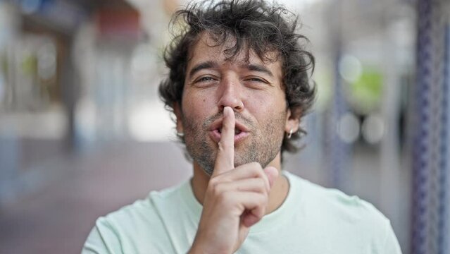 Young hispanic man smiling confident doing silent gesture at street