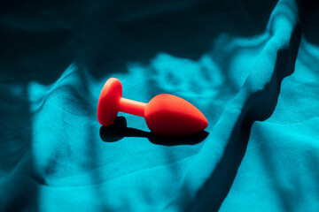 Red silicone anal plug, sex toy, on a blue background in the shade. Contrast photo of anal toys, erotic toys - obrazy, fototapety, plakaty