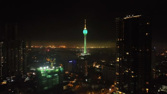 Forwards fly around modern high rise buildings. Aerial view of dominant colour illuminated Lotus Tower at night. Colombo, Sri Lanka