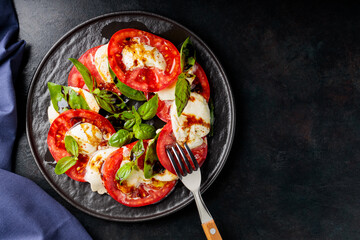 Italian caprese salad with sliced tomatoes, mozzarella, basil, olive oil on dark background. Copy space. Top view