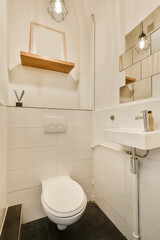 a bathroom with a white toilet and black tiles on the floor next to a mirror above it is a wooden shelf