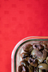 Glass bowl with delicious olives with oil. Background with red tablecloth.