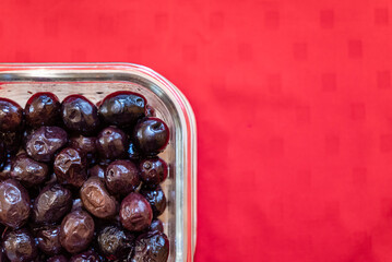 Glass bowl with delicious olives with oil. Background with red tablecloth.