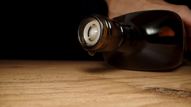 I pick up the empty whiskey bottle from the wooden table, and the last drops are dripping from it. Dolly slider extreme close-up.