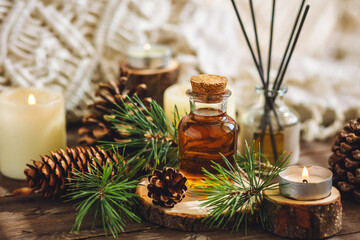 Natural aromatic scented reed diffuser air freshener bottle on wooden table with pine cone, burning candles. Christmas inspiration and mood, cozy home atmosphere, relax. Aromatherapy and decor