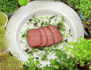 Sliced prosciutto slices on a white plate against a background of microgreens. Veal in spices with...