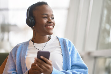Happy African Black teen girl university or college gen z student sitting wearing headphones...