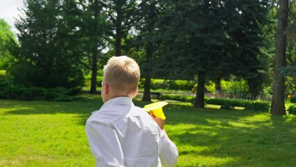 Happy boy playing with paper plane outdoors. Child running in meadow and launching paper plane. Dream concept. Positive male having fun at sunny day. 4K, UHD