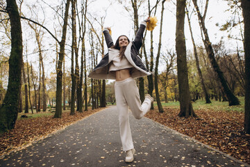 Attractive pretty woman walking outdoor, portrait of young lady in warm sunny autumn park season, fall, hold yellow orange red maple leaves, dressed leather wool fur jacket smiling having fun 
