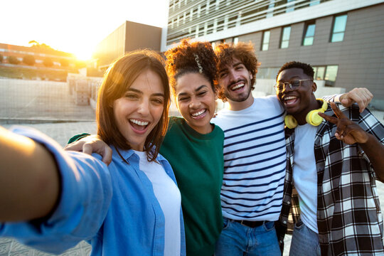 Happy multiracial friends taking selfie and having fun together outdoors in the city during sunset. Looking at camera.