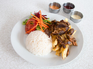Delicioso arroz blanco con mollejitas, papas fritas, ensalada, chicha y salsas sobre un fondo claro. Vista superior, arriba