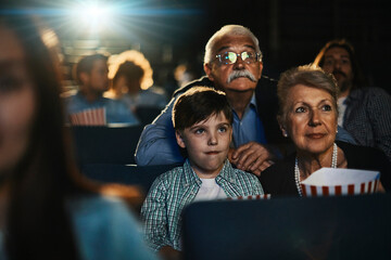 Grandparents and grandson watching a movie in a movie theater and eating popcorn