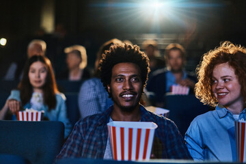 Young mixed couple watching a movie in a movie theater and eating popcorn