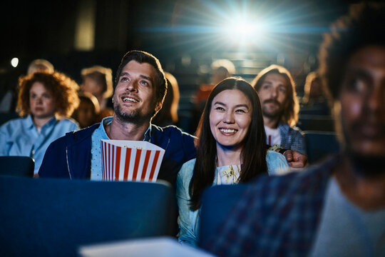 Young couple watching a movie and eating popcorn in a movie theater