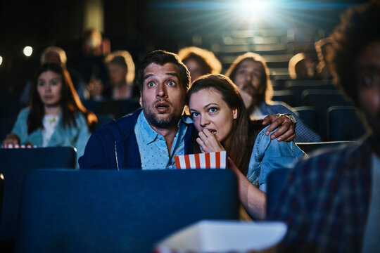 Young couple watching a scary horror movie in a movie theater