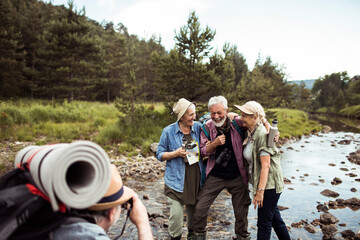 Group of senior people taking a photo with a camera while they are out hiking and preparing to camp in a forest