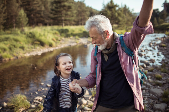 Grandfather and granddaughter hiking by a creek in the forest