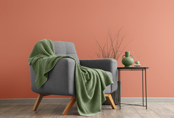 Grey armchair with green plaid and table near color wall in room