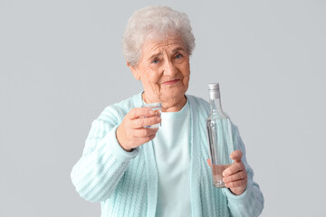 Senior woman with glass and bottle of vodka on light background