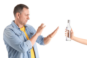 Displeased mature man rejecting bottle of vodka on white background