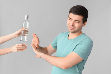 Young man rejecting vodka on light background