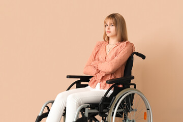 Fototapeta na wymiar Upset young woman in wheelchair on beige background