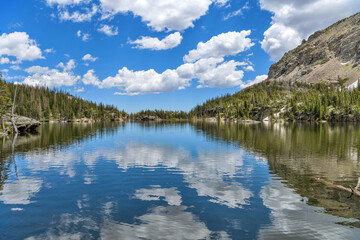 The Loch - A sunny Summer day view of blue sky and white clouds reflecting in calm mountain lake - The Loch, as seen from the west end of the lake towards to its east outlet. RMNP, CO, USA.