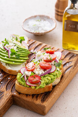 Avocado toasts with radishes, tomatoes and feta topped with olive oil