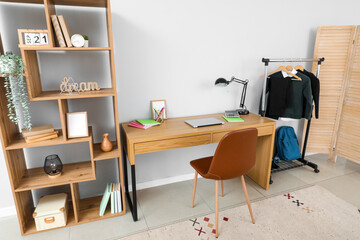 Interior of stylish room with modern workplace and school uniform on rack