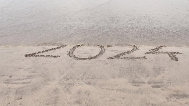 Wave erasing the number 2024 written in the sand.