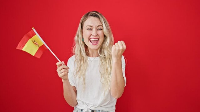 Young blonde woman smiling confident holding spanish flag over isolated red background