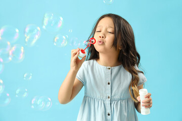 Cute little girl blowing soap bubbles on light blue background