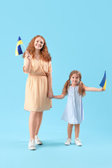 Happy little girl and her mother with Ukrainian flags on blue background