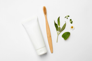 Bamboo toothbrush, tube of cream and herbs on white background, flat lay