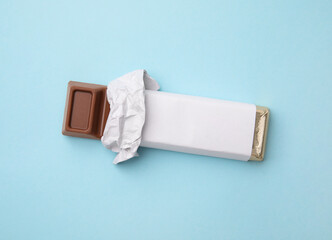 Tasty chocolate bar in package on light blue background, top view