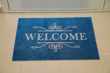 Beautiful blue doormat with word Welcome on floor near entrance
