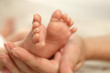 Mother holding her newborn baby, closeup view on feet. Lovely family