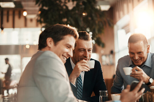 Group Of Businessmen Enjoying A Coffee And Using A Smart Phone After Work In A Cafe Bar Decorated For Christmas And The New Year Holidays