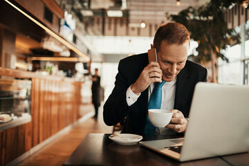 Middle aged businessman having coffee and talking on his phone in a cafe bar decorated for christmas and the new year holidays