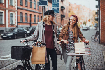 Young lesbian couple shopping and pushing their bicycles on a city street